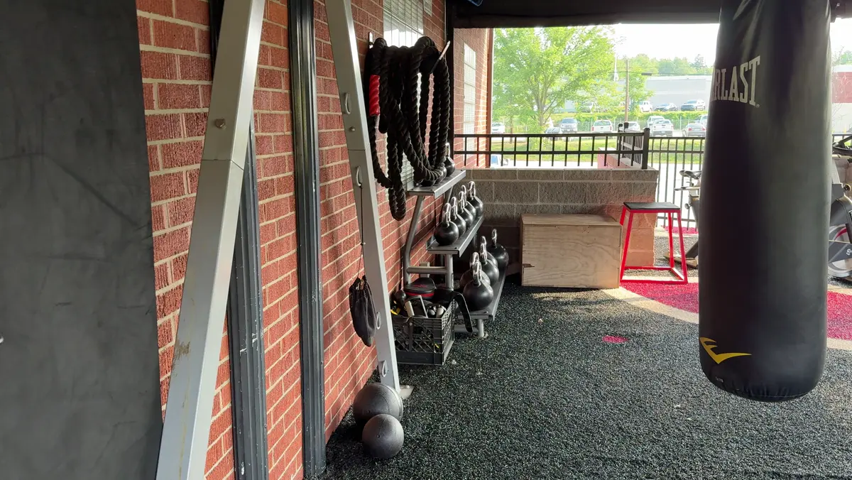 Iron Factory's covered outdoor training deck in Washington, PA — coiled battle ropes and kettlebells against the brick wall, open to the morning air over the treeline